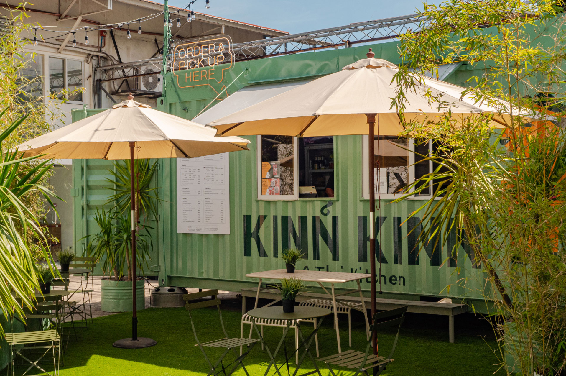 A photo of Kinn Kinn's shipping container kitchen exterior surrounded by trees and outdoor tables and chairs